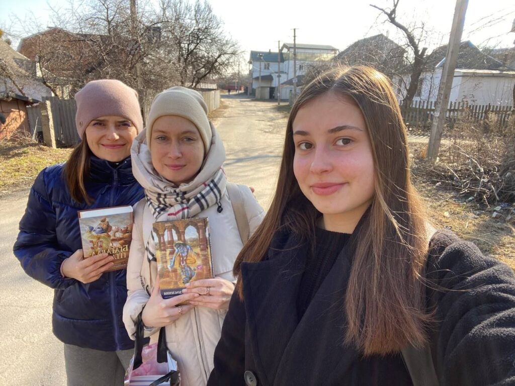 Three devotees distributing spiritual books outdoors